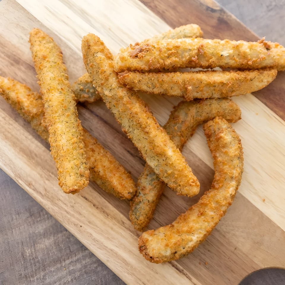 Golden brown fried pickle spears, coated in breading and dill, arranged on a wooden cutting board.
