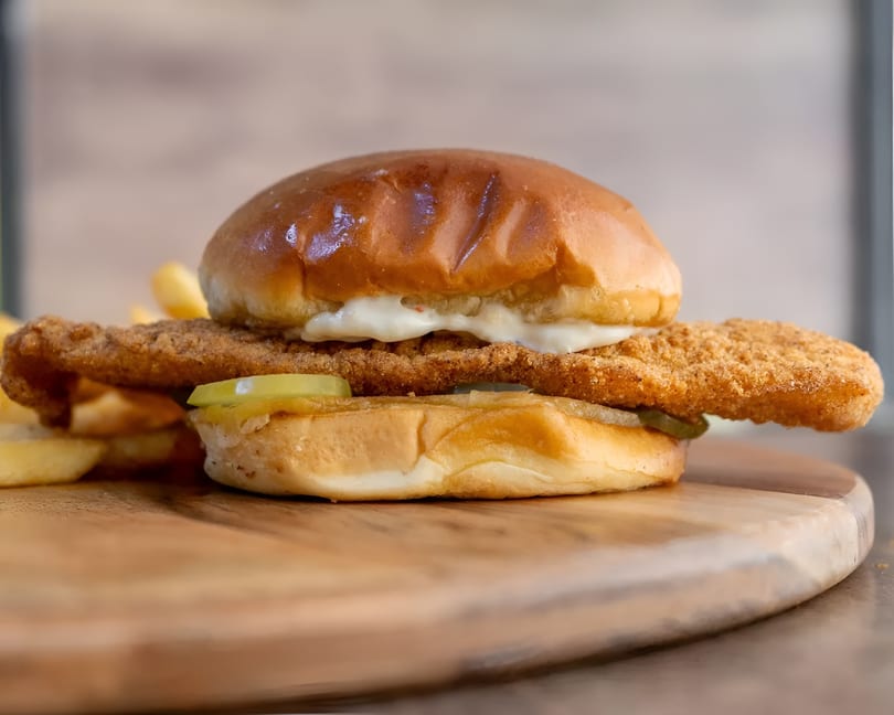Crispy fried fish sandwich with pickles and tartar sauce on a brioche bun, served with fries.