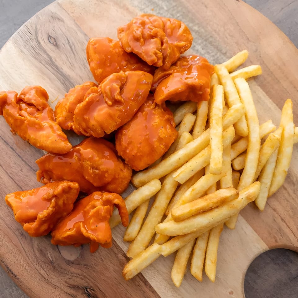 Buffalo chicken tenders and golden french fries served on a rustic wooden board.