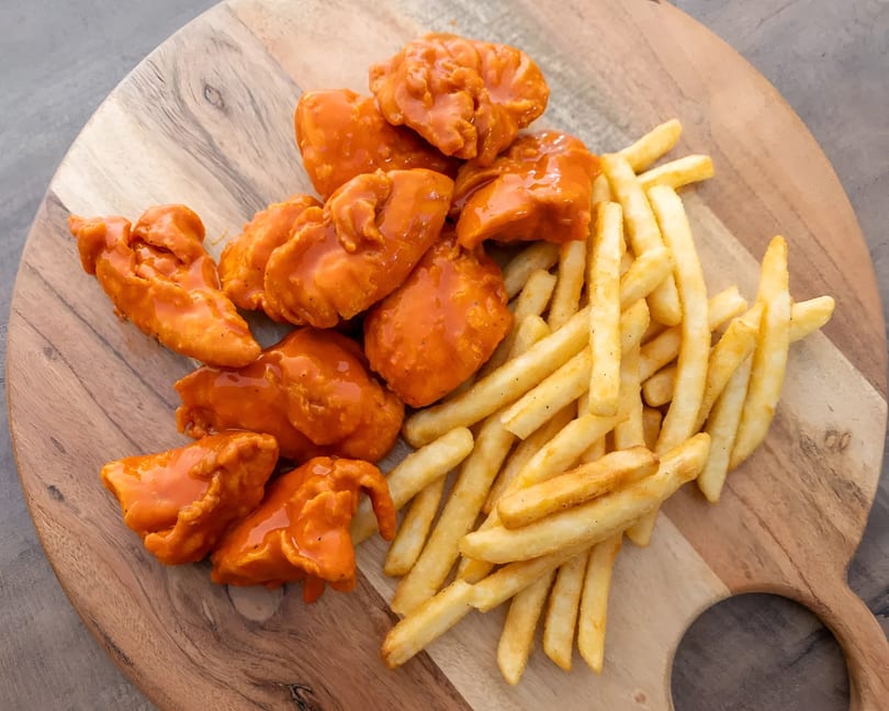 Buffalo chicken tenders and golden french fries served on a rustic wooden board.