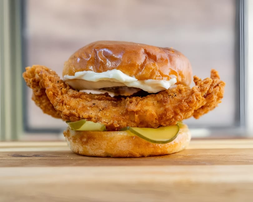 Crispy fried chicken sandwich with pickles and mayonnaise on a brioche bun, on a wooden board.