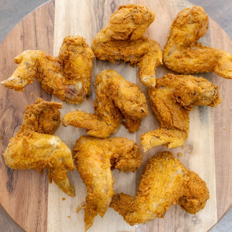 Crispy golden-brown fried chicken wings arranged on a round wooden serving board.