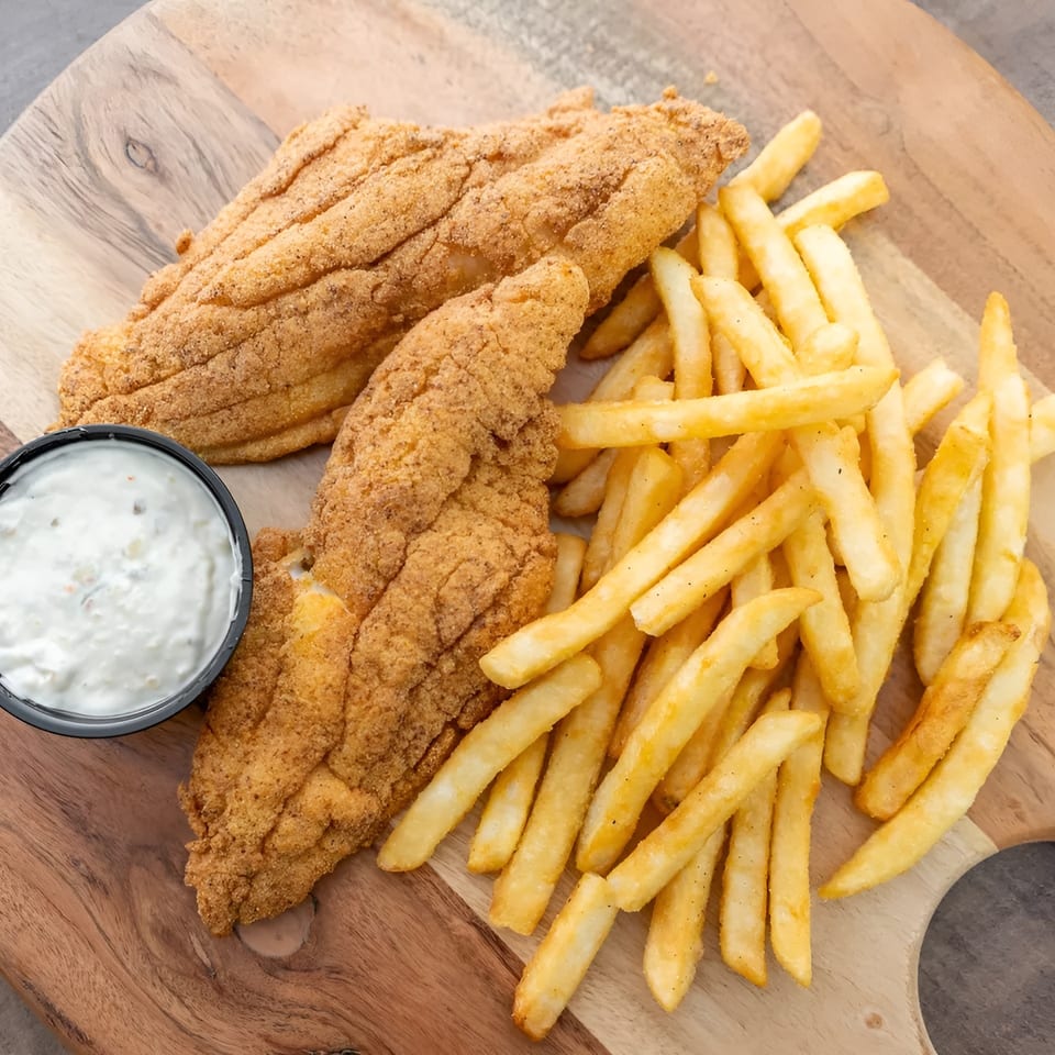 Two pieces of fried fish, a side of french fries, and tartar sauce on a wooden board.